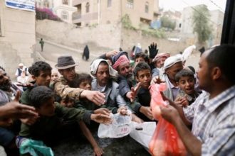 People gather to collect food rations at a food distribution center in Sanaa, Yemen. (c) REUTERS